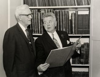 Photo of two men looking at a large book. 