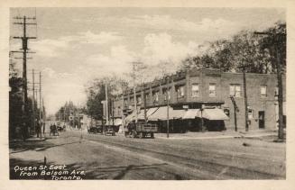 Picture of street with store buildings on right and streetcar tracks and vehicles. 