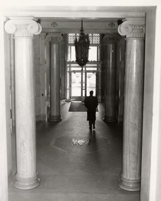 A photograph of a hallway in an office building, with a person walking away from the camera tow ...