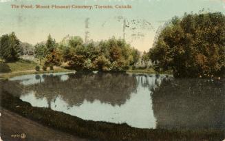 Colour postcard of a pond surrounded by trees. The caption on the top front states, "The Pond,  ...