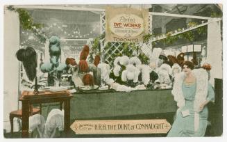 Colorized photograph of a woman standing in front of a shop counter full of dyed ostrich feathe ...