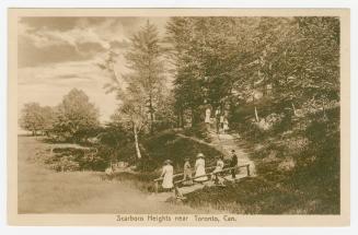 Picture of people standing on a bridge and others walking up a steep trail in a wooded park. 