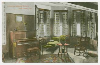 Picture of a living room with piano, large curtained windows and chairs. 
