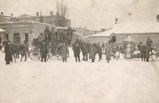 A photograph of a group of firemen standing in front of some buildings and with horses reined t ...