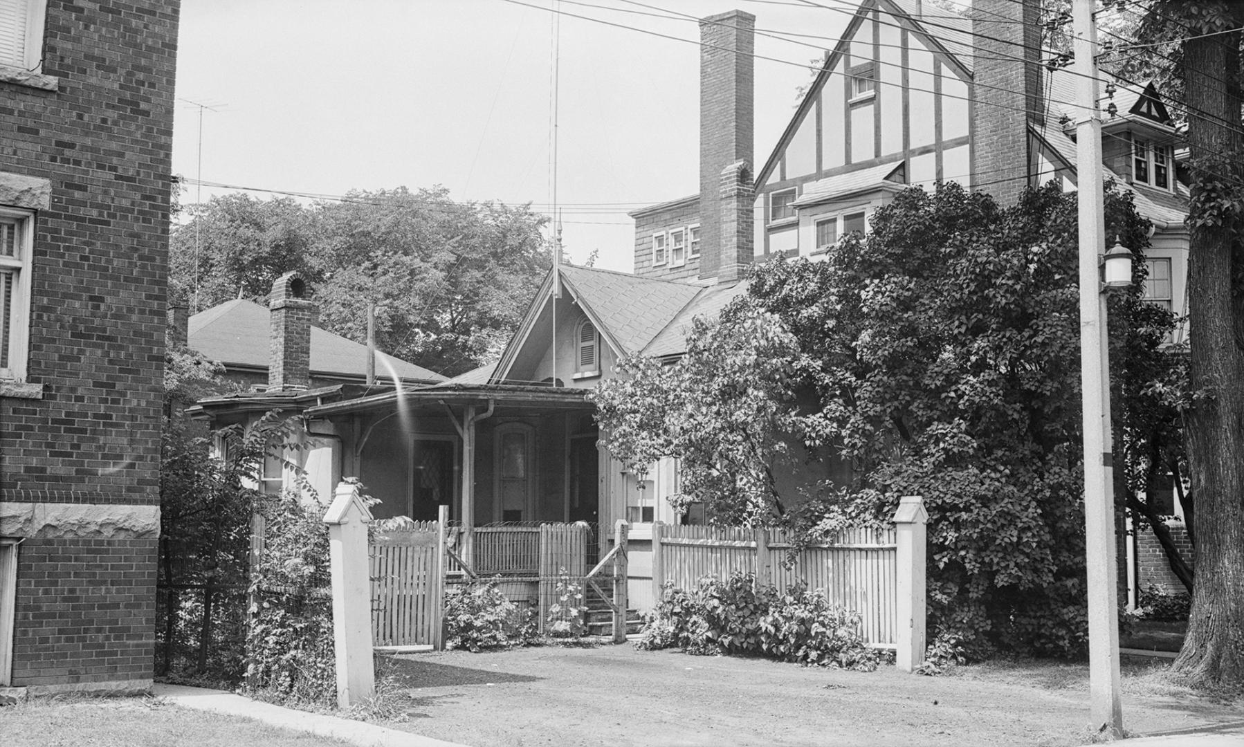 A photograph of a house, with a small tree in front of it and a fence, gate and driveway in fro ...
