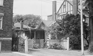 A photograph of a house, with a small tree in front of it and a fence, gate and driveway in fro ...