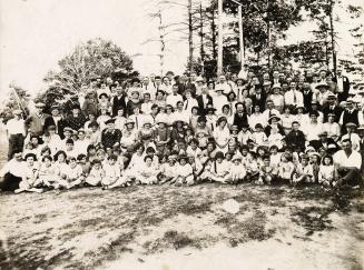 Photograph of a large group of people posed for a group photo in a park with trees in the backg ...