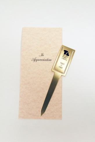 A brass letter opener with the old Toronto Public Library logo printed on it, inserted into a p ...