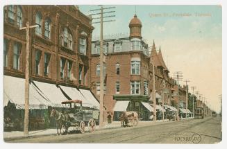 Picture of a street with buildings on one side and horse drawn delivery wagons. 