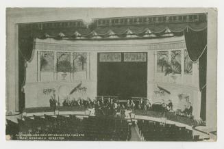 Picture of interior of a theatre with orchestra members. 