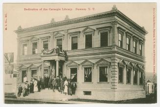Picture of large stone library building with group of people on the front steps. 