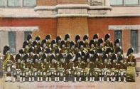 Colorized photograph of a large marching band in Scottish dress posing in front of a castle-lik…