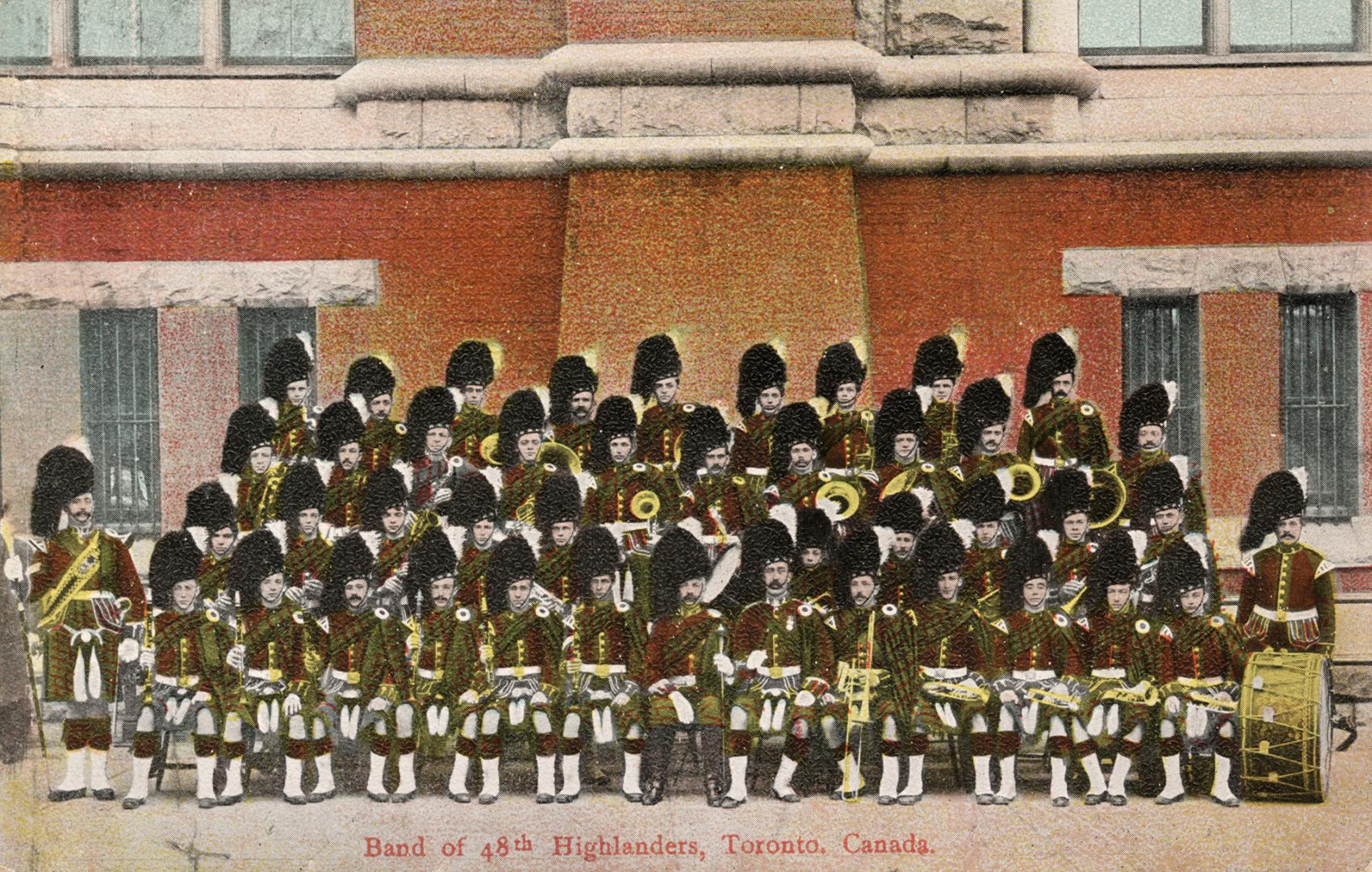 Colorized photograph of a large marching band in Scottish dress posing in front of a castle-lik ...