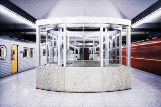 A photograph of a subway platform. In the middle of the platform there is a waiting area with s ...