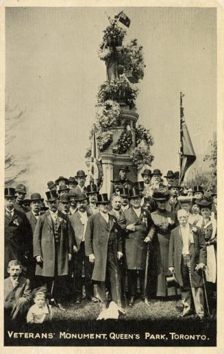 Picture of a large monument covered in flowers with crowd in front. 
