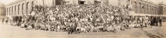 A panoramic photograph of a large group of people posing in front of an office or industrial bu ...