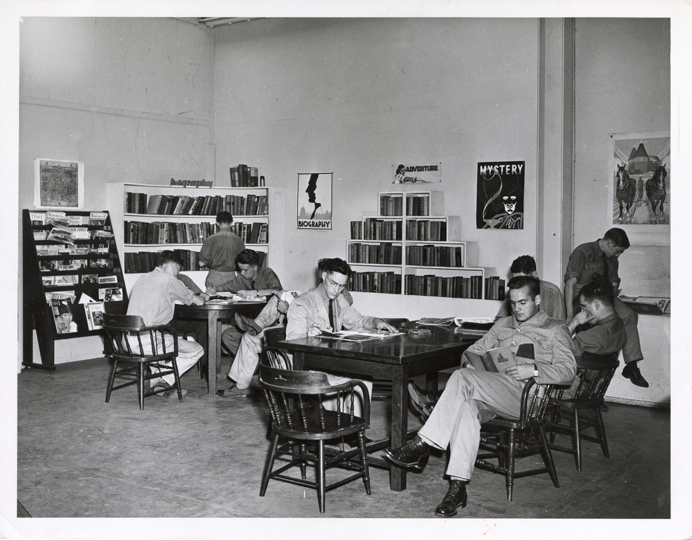 Photo of men reading at tables in a library. 