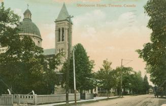 Colorized photograph of a city street bordered by large houses, trees and a big church.