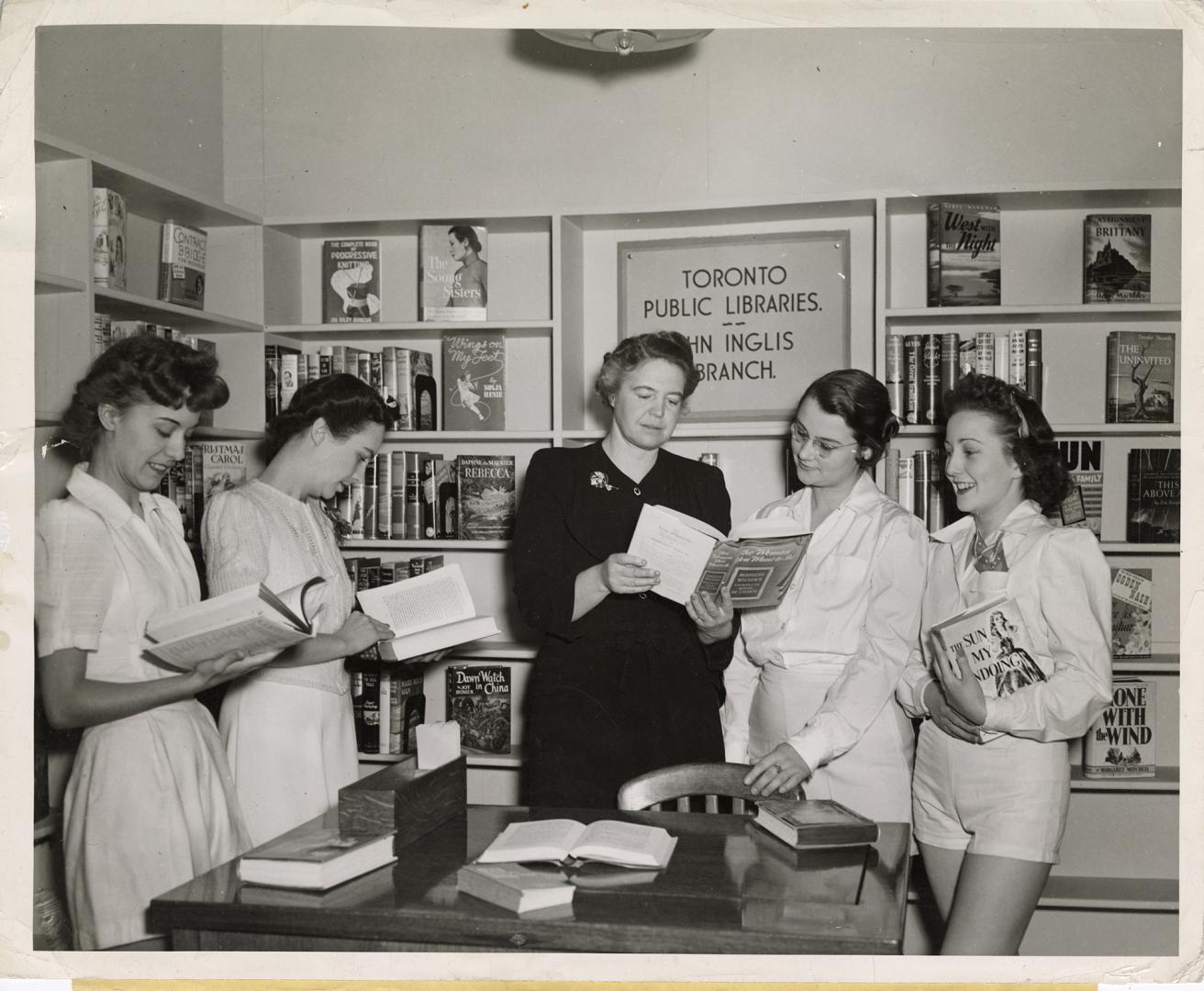 Photo of a librarian showing a book to four girls in a library. 