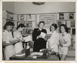 Photo of a librarian showing a book to four girls in a library. 