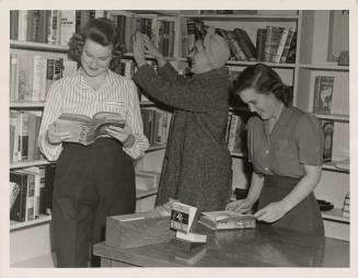 Photo of three girls looking at books in a library.