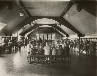 Photo of children reading at tables and looking at books on shelves in a large library room. 