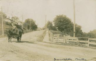 Sepia toned photograph of a horse drawn cart on a country road.