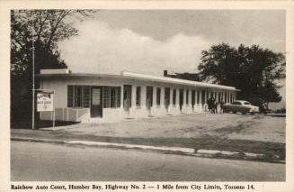 Black and white photo postcard depicting an image of motel with a car and people standing in th ...