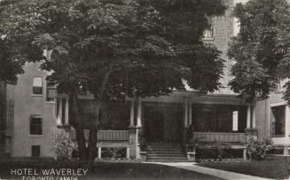 Black and white photo postcard depicting an image of a large house with a front porch being use ...