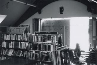 Photo of book shelves and large window with hoarding in background. 