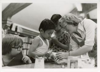Photo of children at a table with library staff member making puppets. 