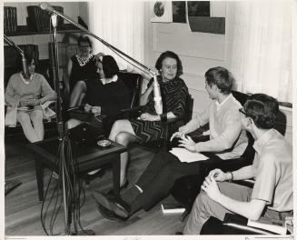 Photo of four young people and two adults sitting talking and large microphones in front of the ...