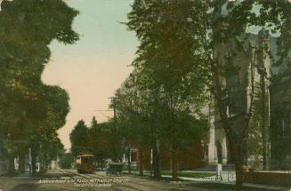 Colorized photograph of a street card on a tree lined road in front of a large church.