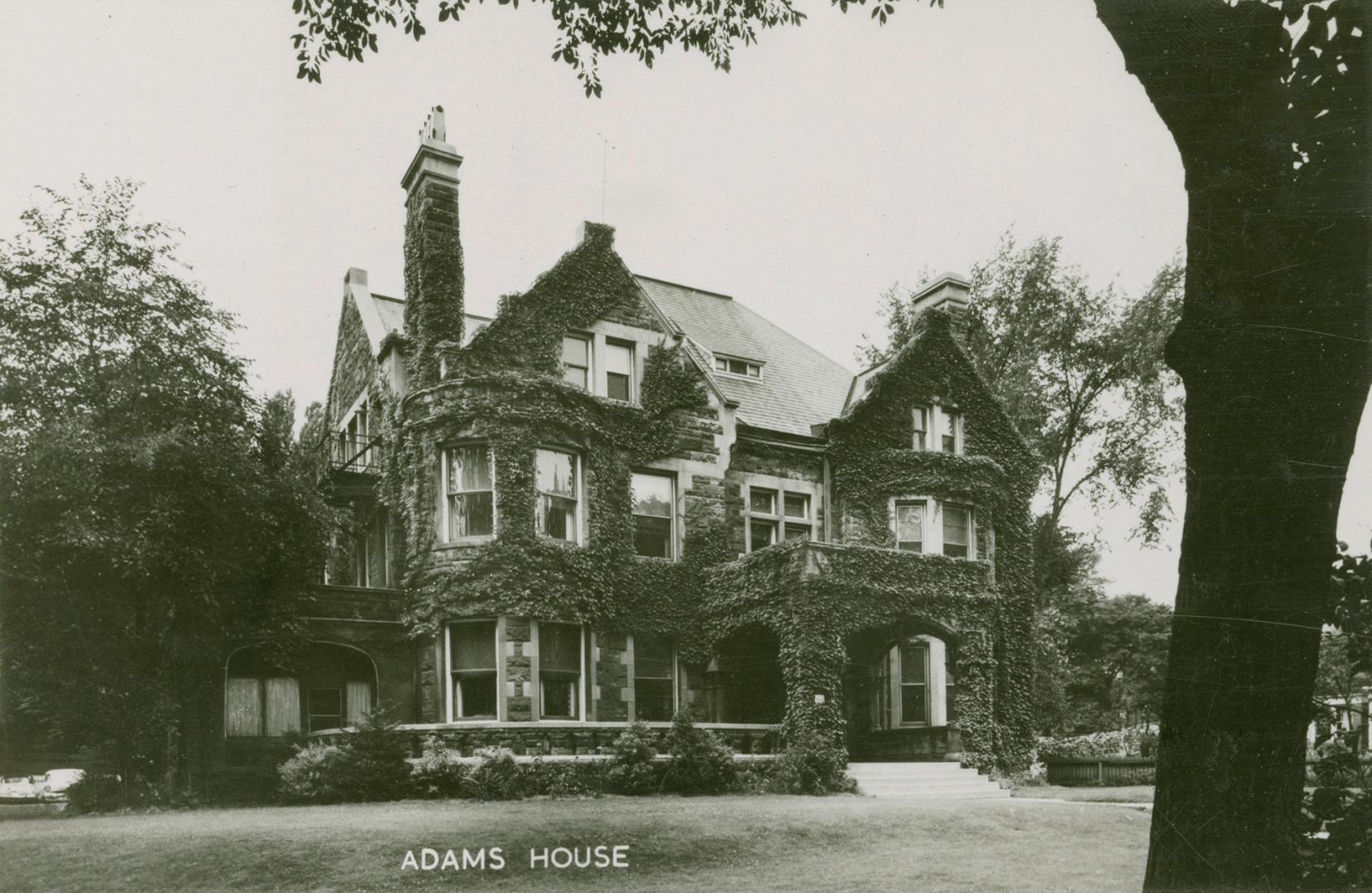 Black and white photograph of a huge house covered in ivy.