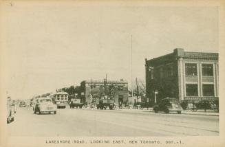 Black/white photo postcard depicting Lakeshore Road at street level with cars and a trolley car ...