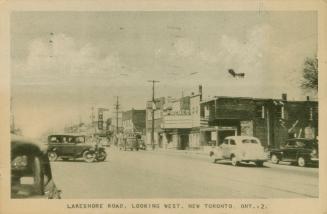 Black/white photo postcard depicting Lakeshore Road at street level with cars going by. Caption ...
