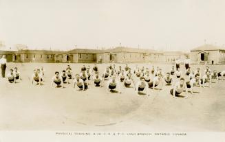 Sepia-toned photo postcard depicting a team of men doing push-ups in front of army barracks at  ...