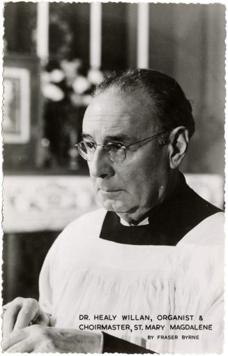 Black and white head shot of a man wearing glasses in a choir gown.