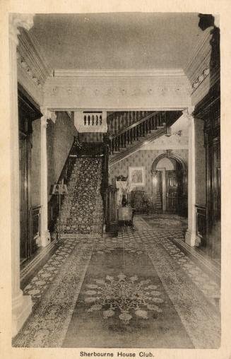 Black and white photograph of the the interior front hall of a large house.