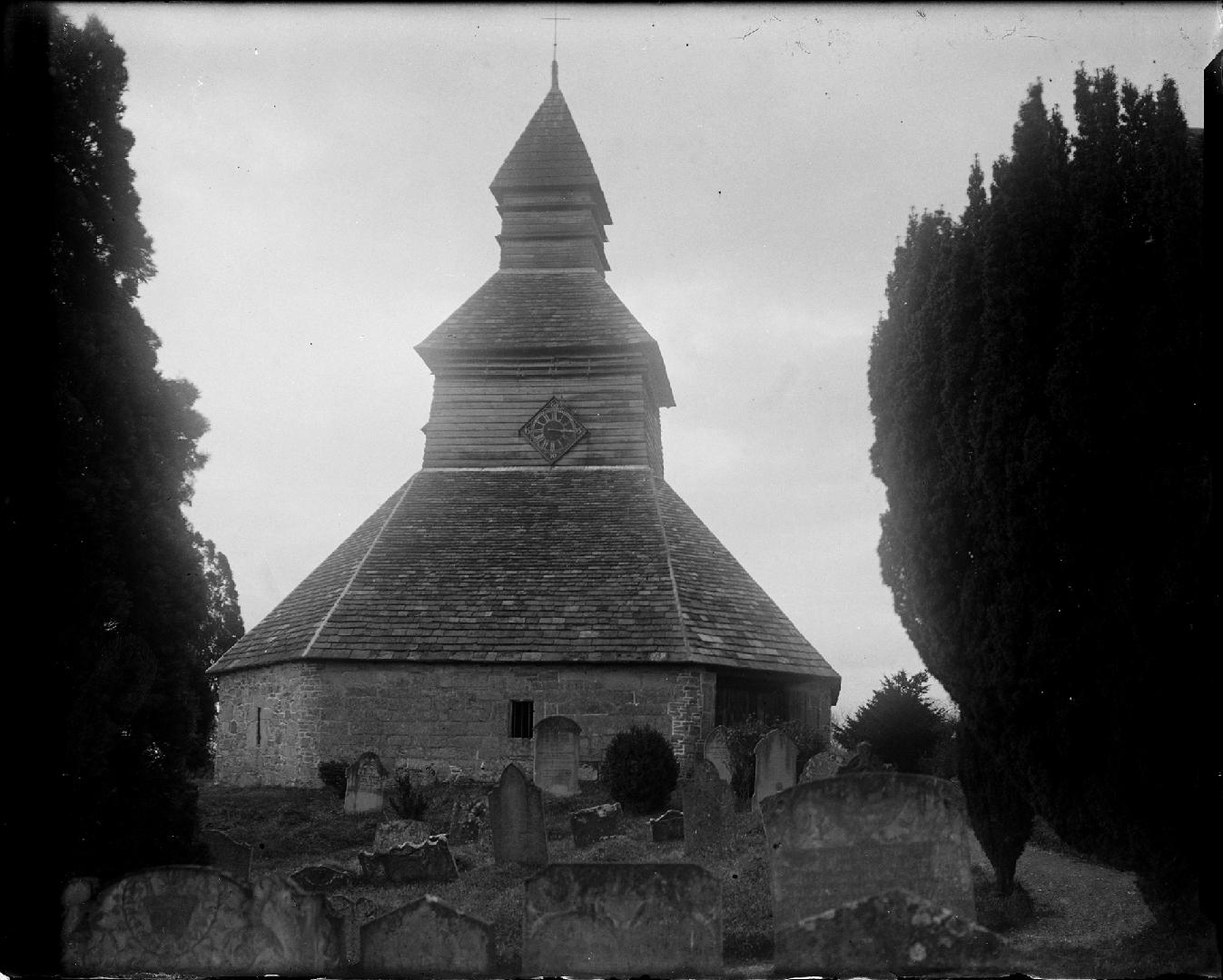 A photograph of a belfry, with a clock on the side facing the photographer. There are graveston ...