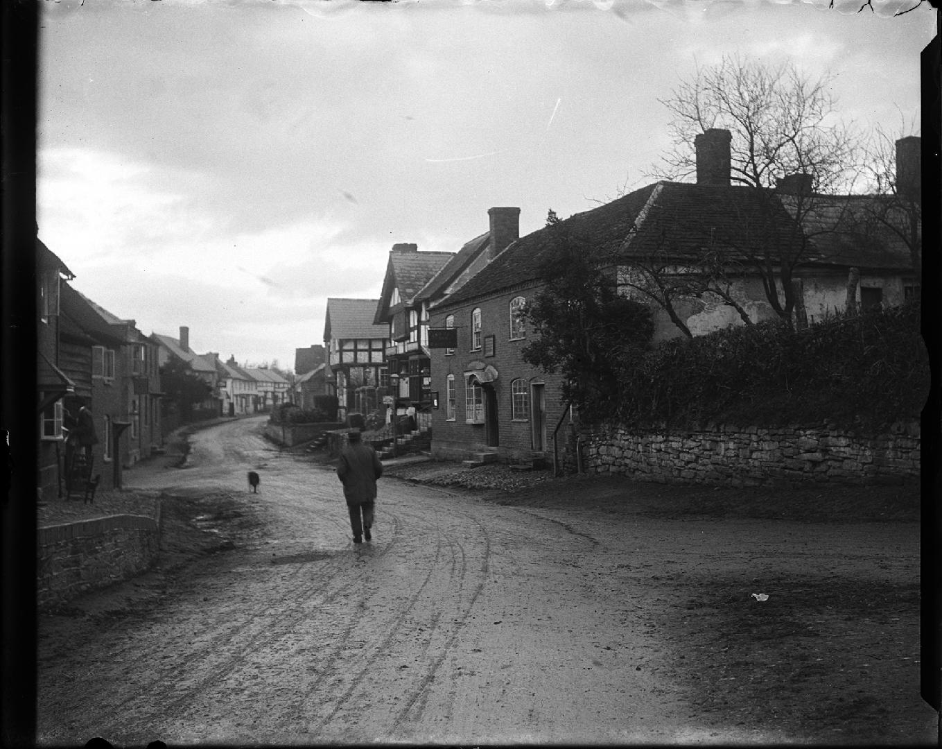A photograph of a city street, with a muddy dirt road winding through a neighbourhood with two  ...