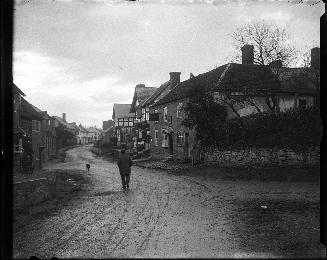 A photograph of a city street, with a muddy dirt road winding through a neighbourhood with two …