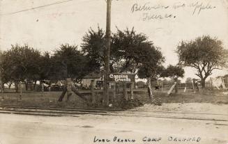 Sepia-toned photo postcard depicting a camping facility with streetcar tracks running across th ...
