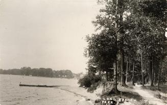 Black and white photo postcard depicting a pathway through a forest alongside a shoreline and s ...