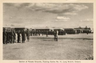 Sepia-toned photo postcard depicting men lined up on a large field in front of the barracks at  ...