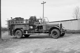 A photograph of a truck with water pumping equipment in its flatbed. The truck is parked on a d ...
