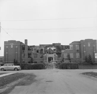 A photograph of a large school displaying damage from a fire. The middle of the building and th…