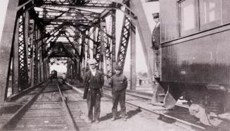 A photograph of a railway bridge, with two people standing between the two sets of tracks on th ...