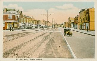 Colorized photograph of a city street with buildings on each side of it, automobile in the midd…