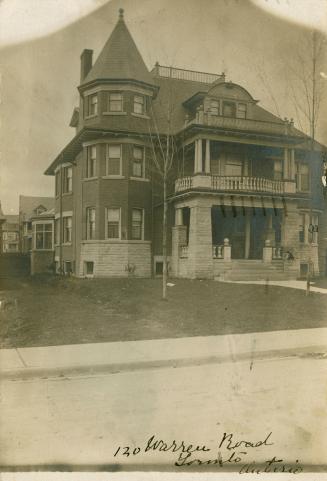 Black and white photograph of a substantial three story house with a turret and balconies.
